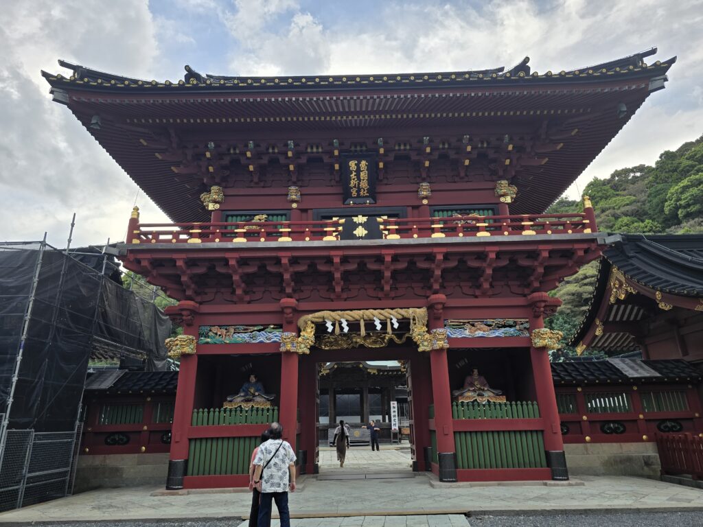 Ornate red and gold wooden gate of Kunōzan Tōshōgū Shrine in Shizuoka, with detailed carvings and visitors entering
