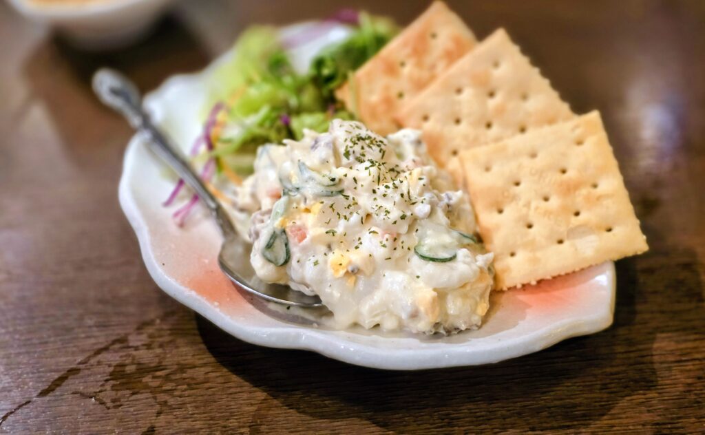 Japanese-style potato salad served with leafy greens and salted crackers on a side dish.