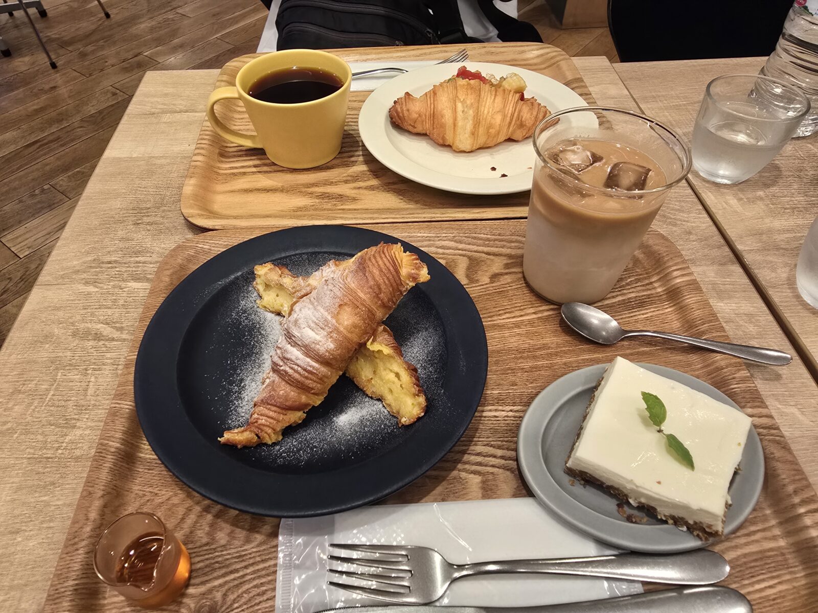 A modern café morning set , with croissants, coffee, iced lattes, and dessert on wooden trays.