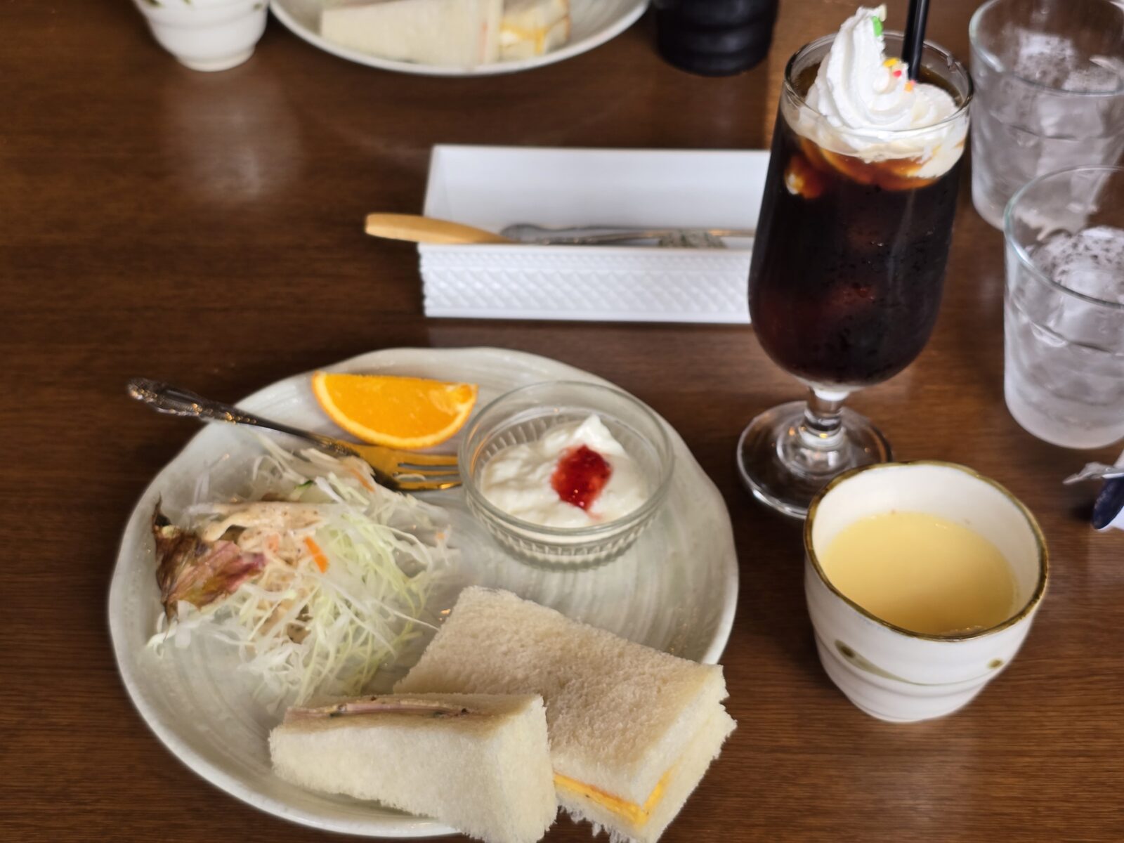 Japanese morning set meal in Gifu, featuring sandwiches, salad, yogurt, an orange slice, corn soup, and a tall iced coffee with whipped cream.