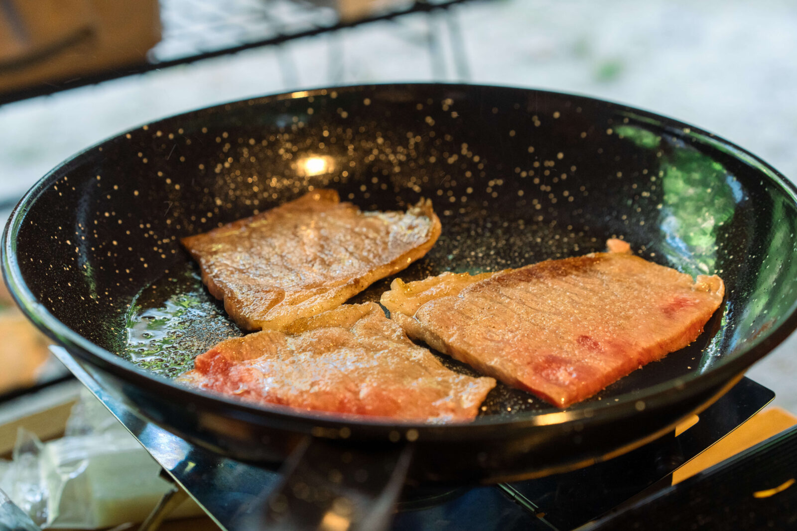 Slices of beef sizzling in a frying pan over a camping stove in Gifu, Japan