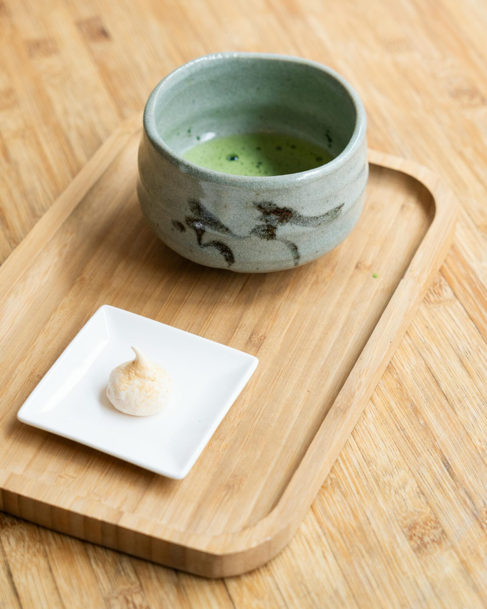 A traditional Japanese tea set featuring a bowl of matcha and a small wagashi sweet on a wooden tray, representing the harmony and thoughtfulness of tea culture.