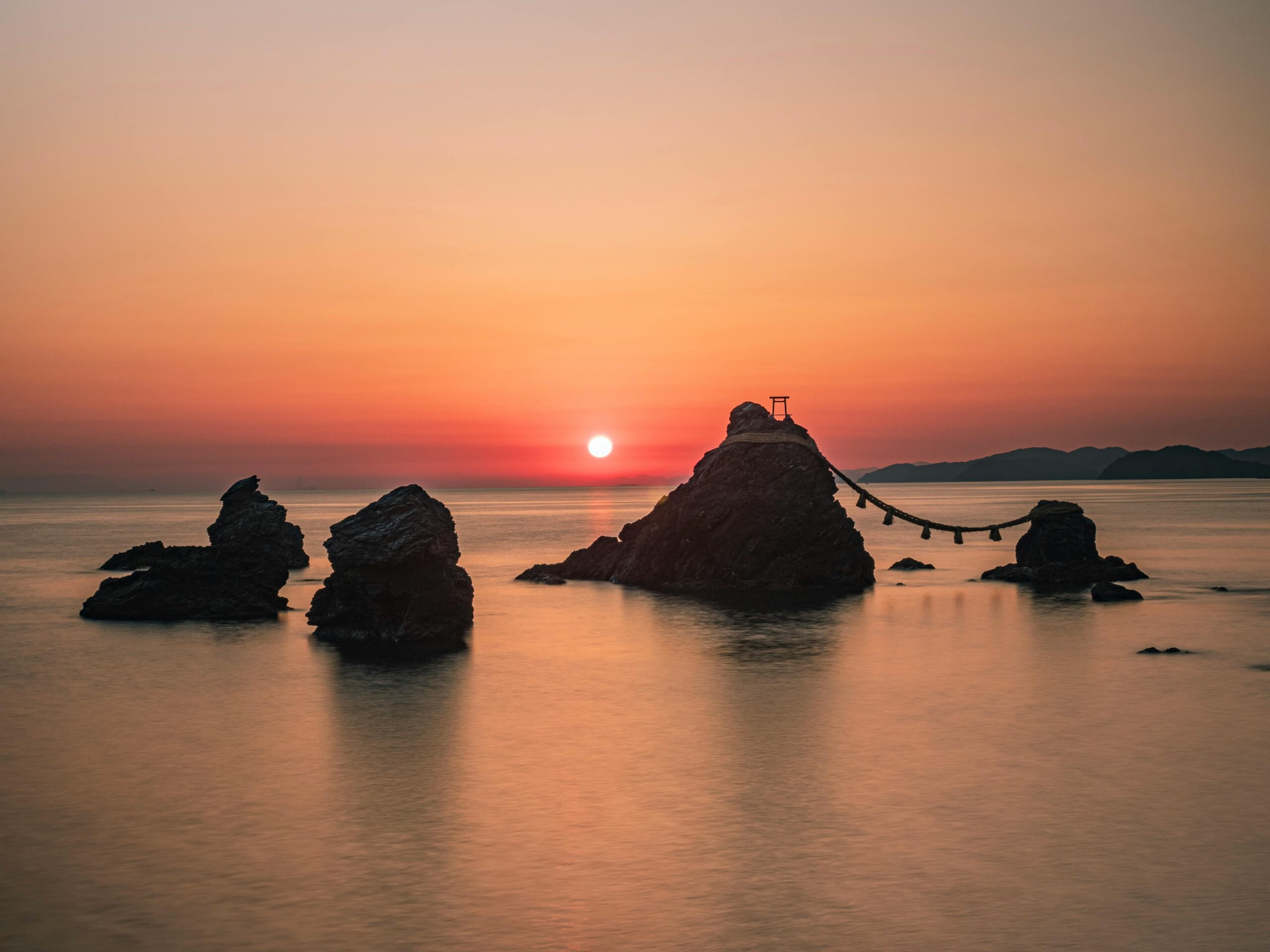 Sunrise over the Meoto Iwa sacred rocks connected by a Shinto rope in Japan, symbolizing harmony and new beginnings.