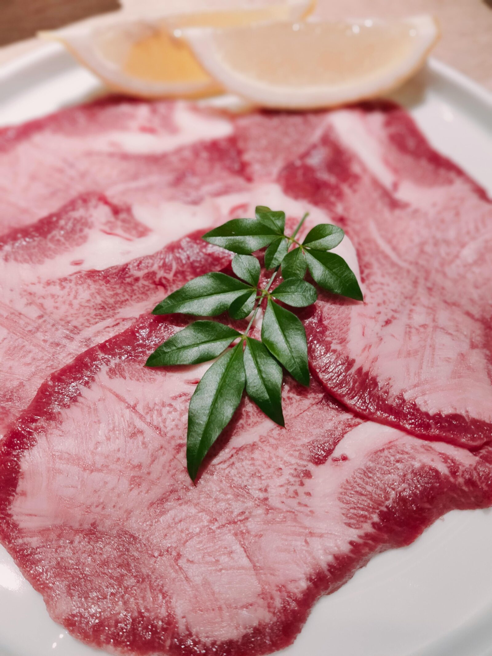 Thinly sliced raw beef tongue with lemon wedges and garnish, a classic dish for yakiniku in Japan