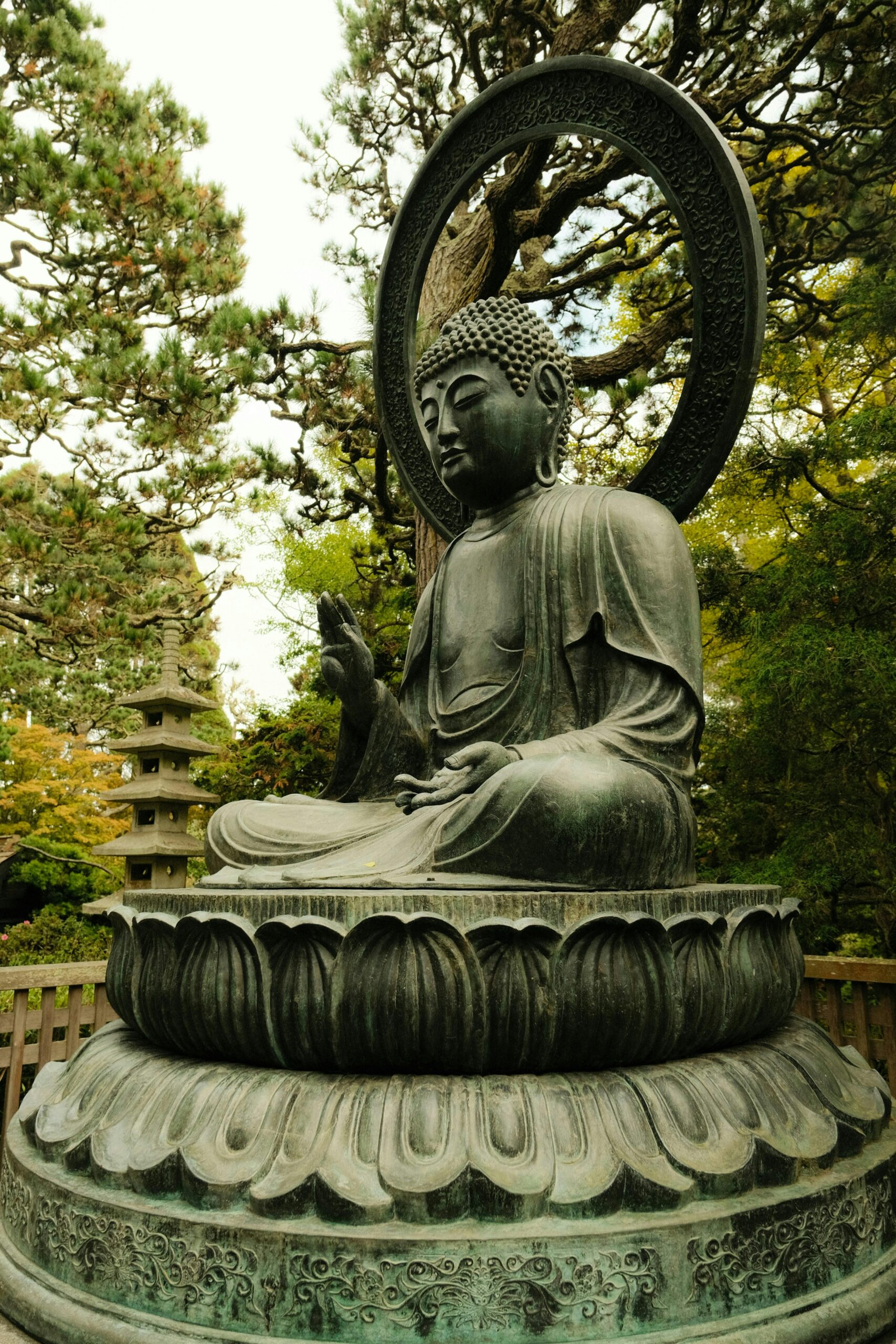 A peaceful bronze Buddha statue seated on a lotus pedestal surrounded by green pine trees at a Japanese temple garden, symbolizing serenity and mindfulness.