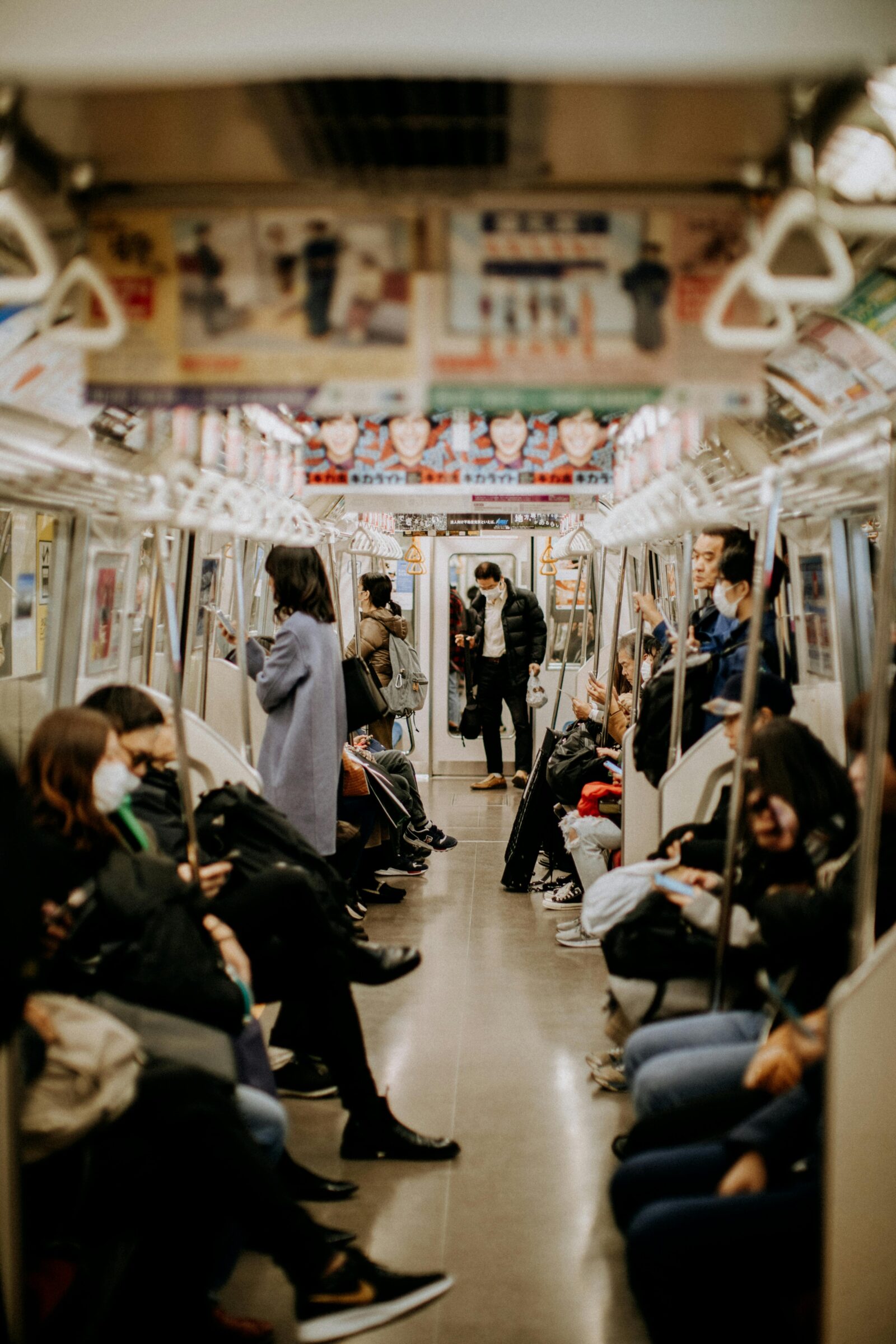 Interior of a Japanese subway train with masked passengers sitting and standing, quietly using their phones.