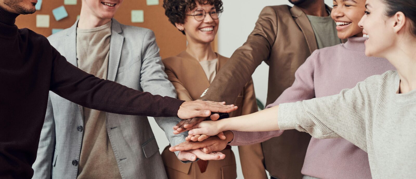 A group of diverse coworkers standing in a circle with their hands stacked together, smiling and showing teamwork in an office setting.