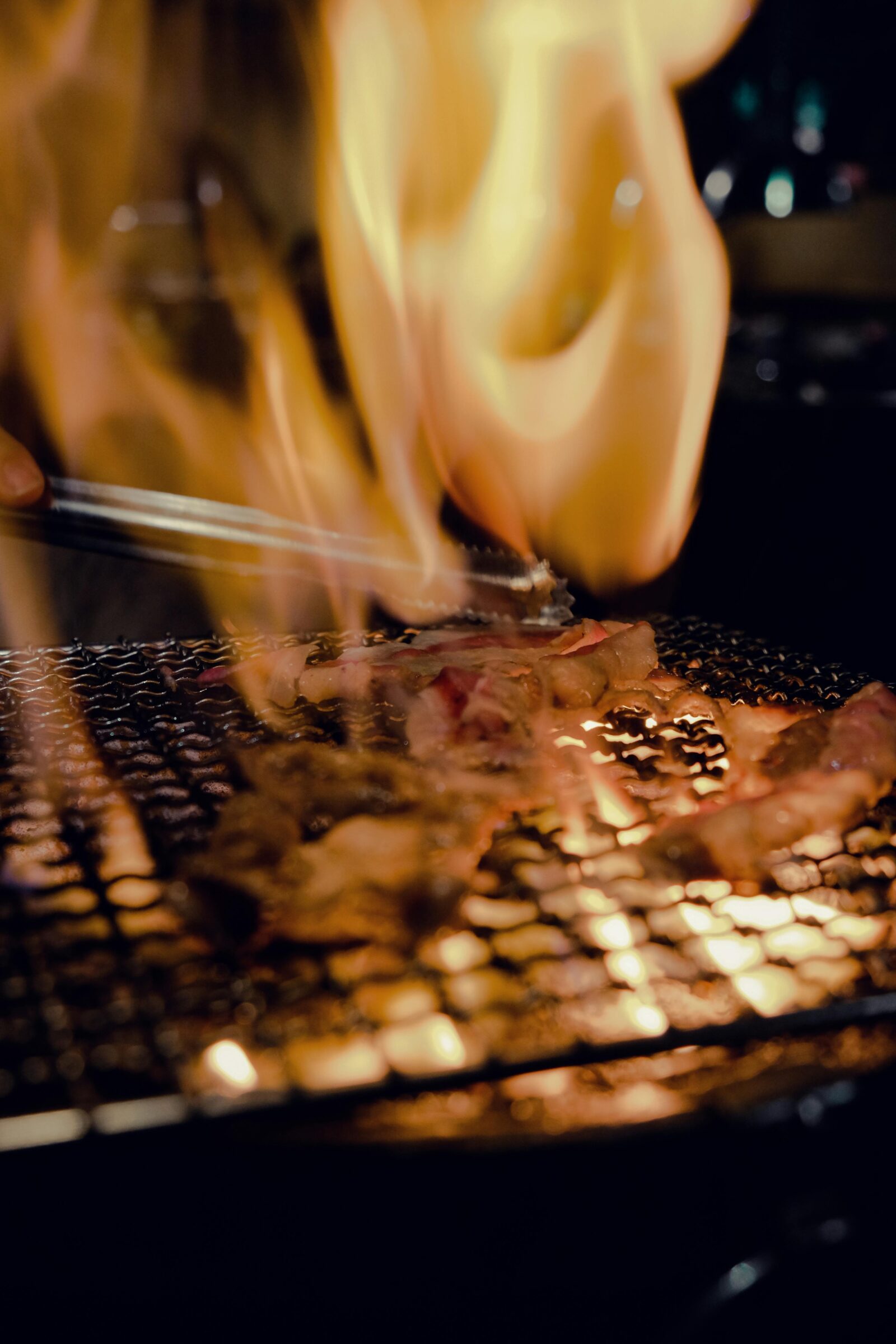 Beef slices grilling over charcoal with flames rising, a lively yakiniku barbecue scene.