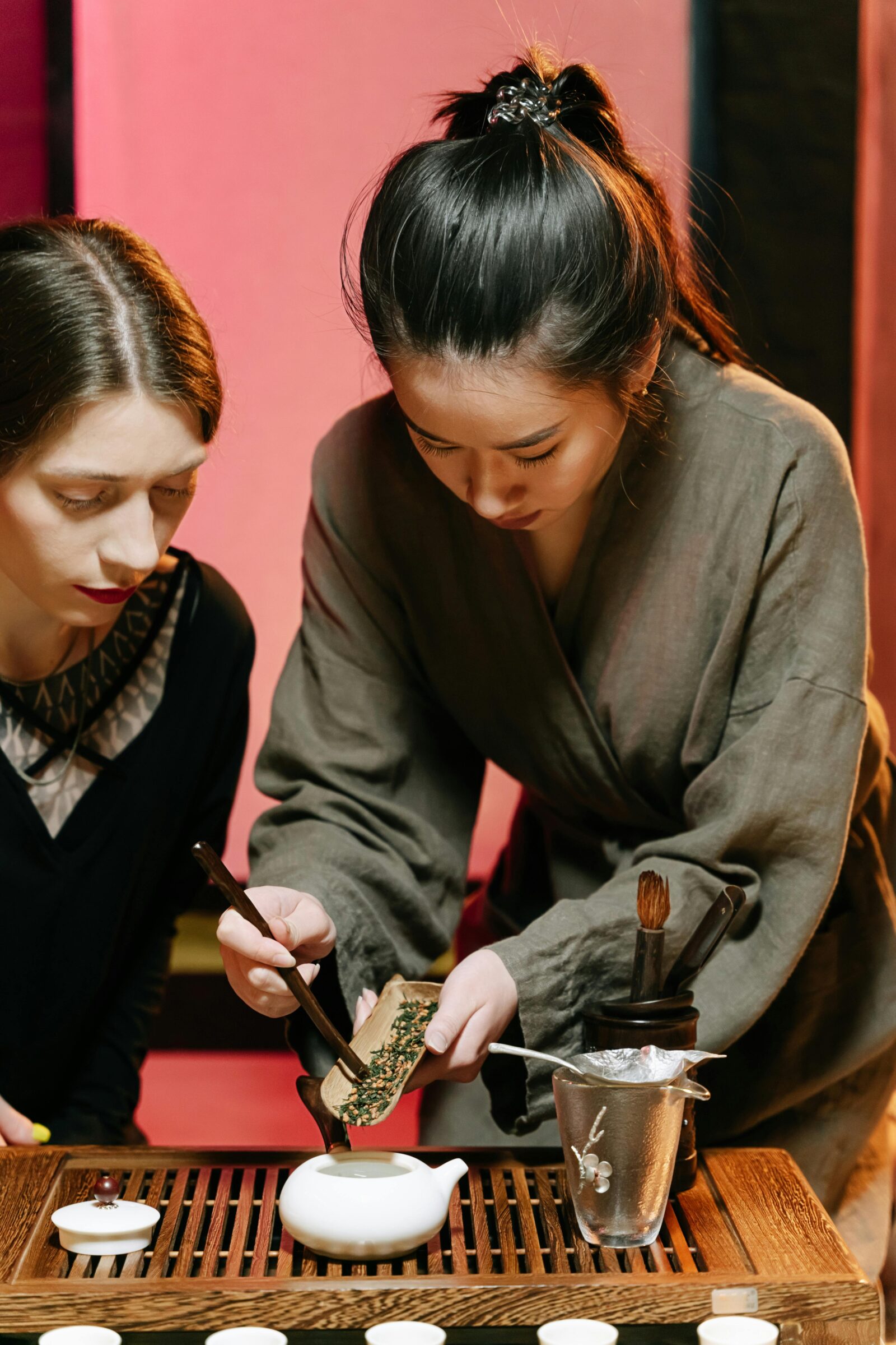 A Japanese woman in traditional attire demonstrating a tea-making process to a guest, showing the precision and grace of Japanese tea culture.