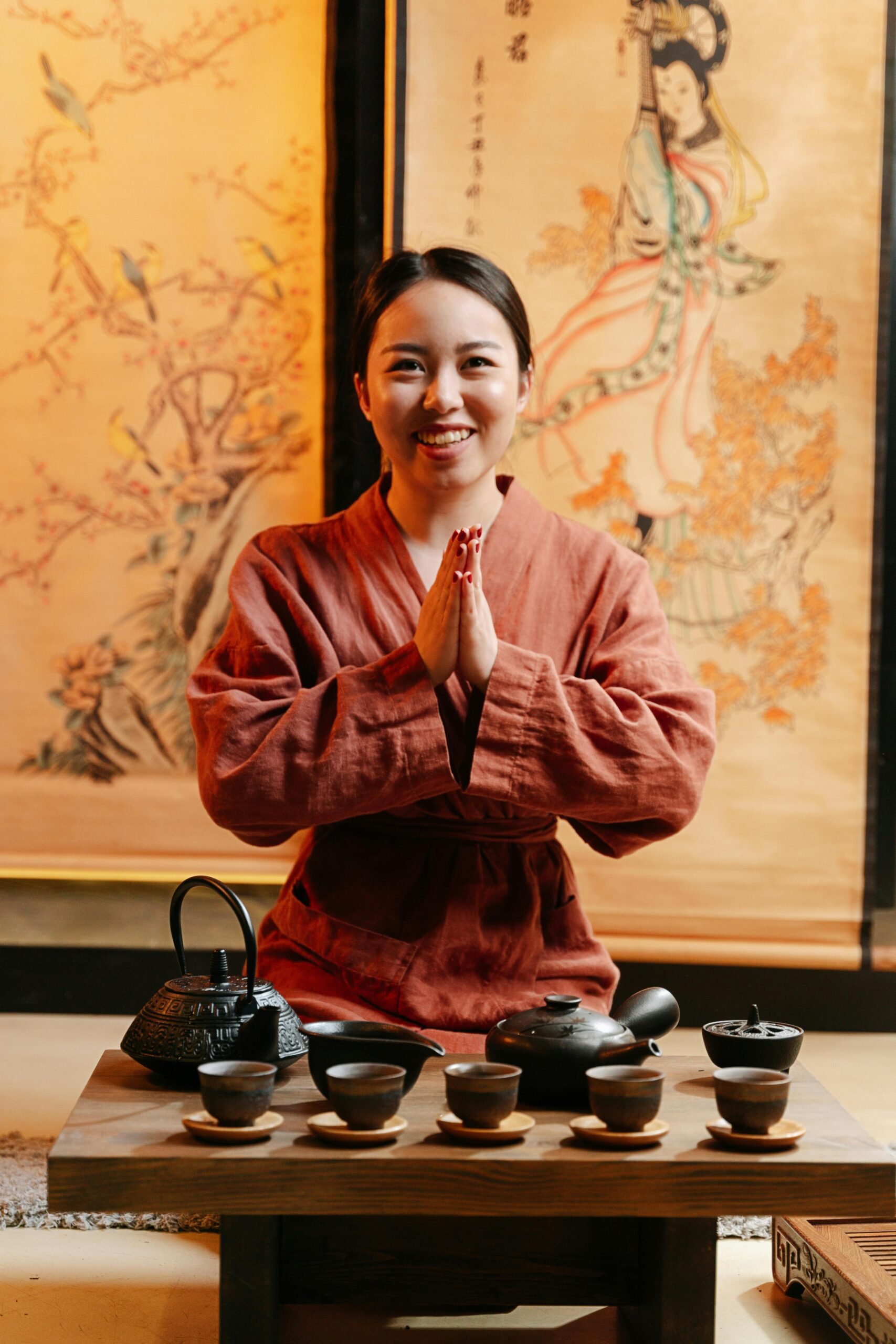 A smiling woman dressed in traditional Japanese attire, welcoming guests with a respectful gesture beside a beautifully arranged tea set, embodying the spirit of omotenashi.