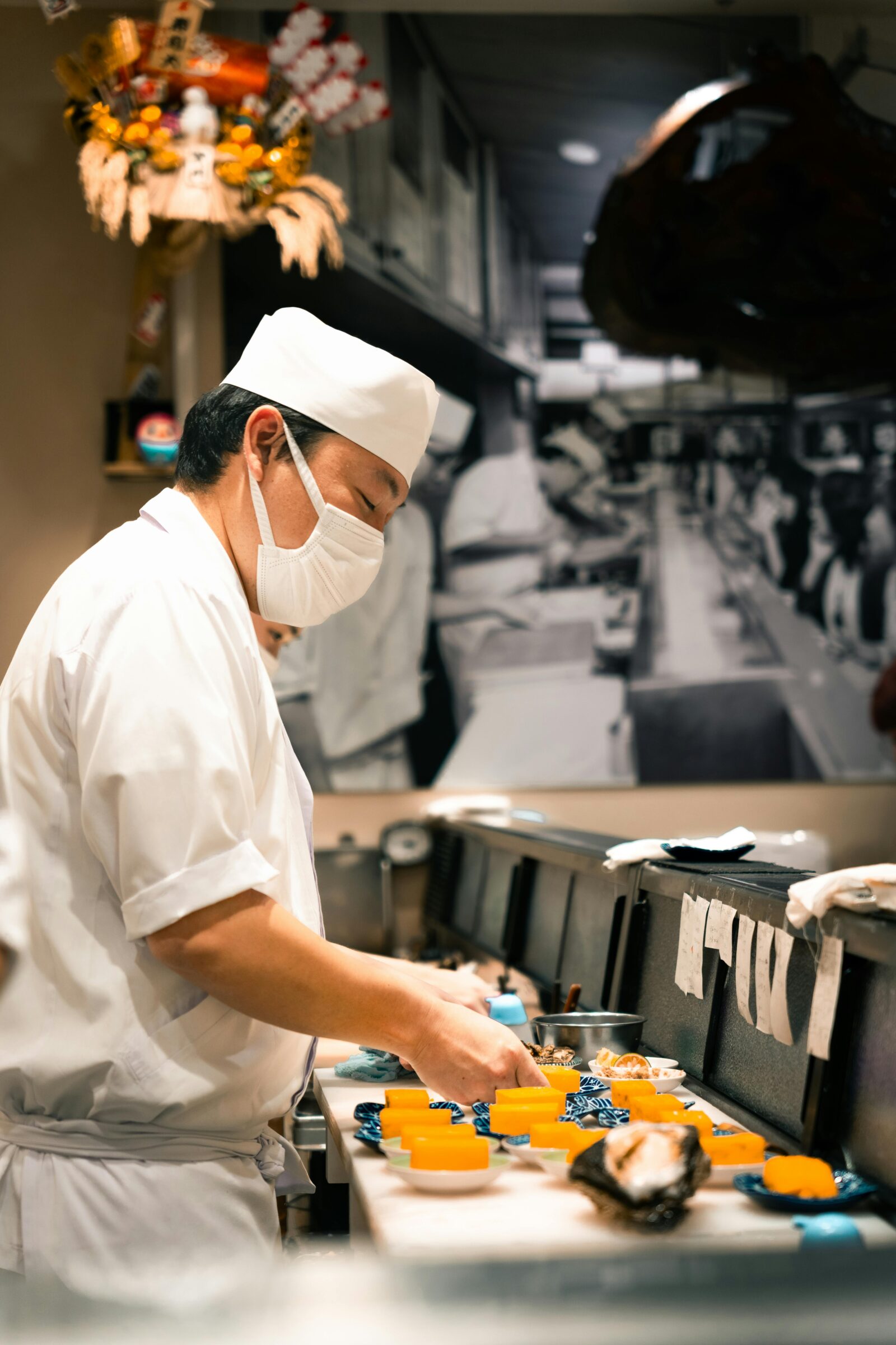 A Japanese sushi chef carefully preparing dishes behind the counter, wearing traditional attire and mask, representing craftsmanship and dedication to detail.