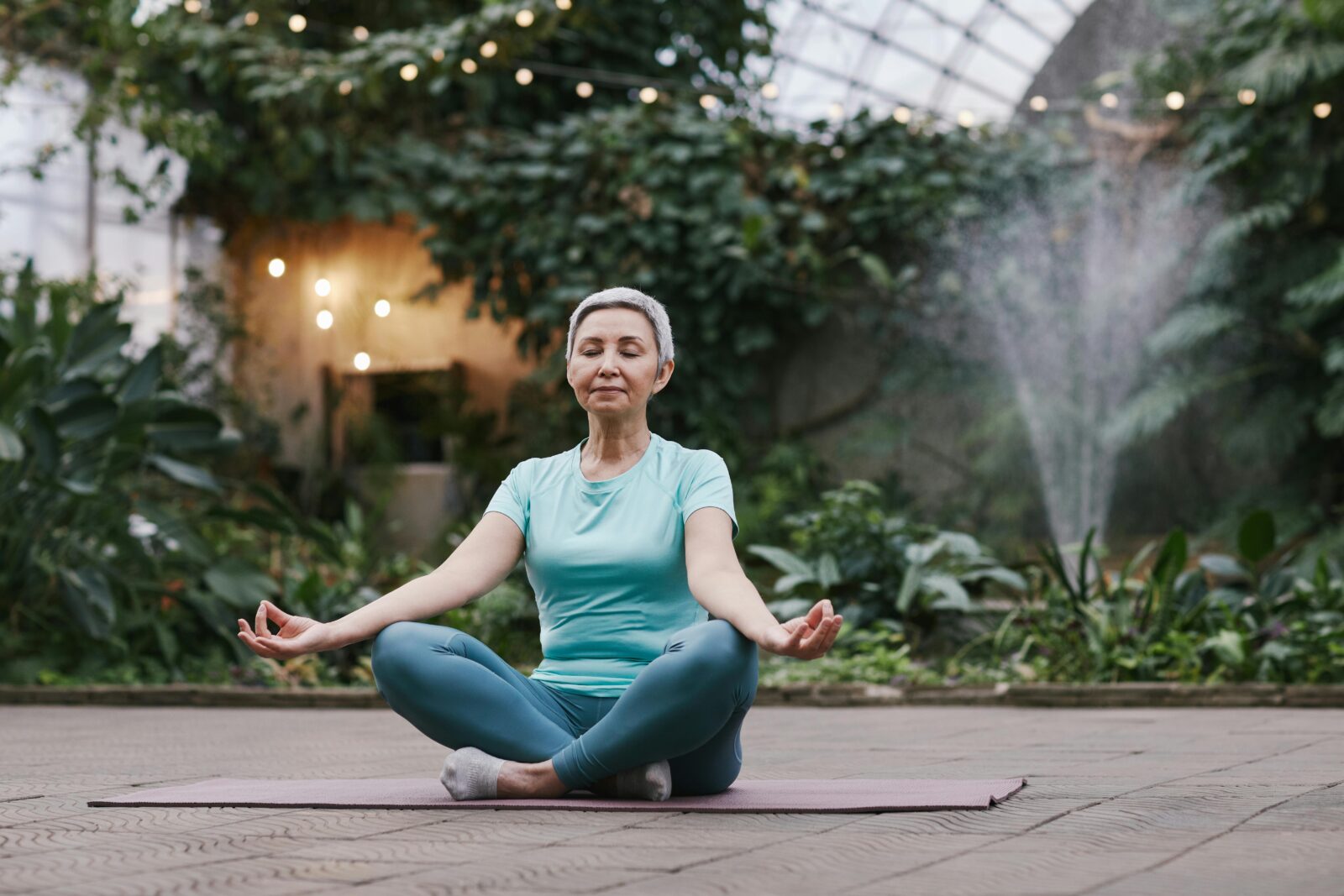 An elderly woman sitting cross-legged and meditating in a peaceful garden, representing wellness, balance, and active aging in Japan.