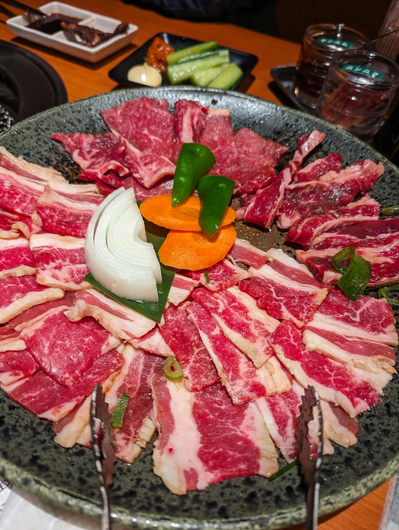 A large plate of assorted raw beef cuts with onion, carrot, and peppers, prepared for yakiniku dining.