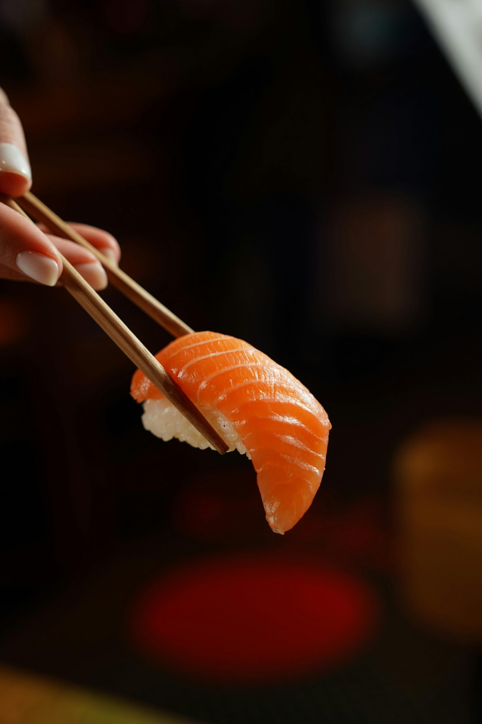 Close-up of hand holding a piece of salmon sushi with wooden chopsticks, representing Japanese dining etiquette and precision.