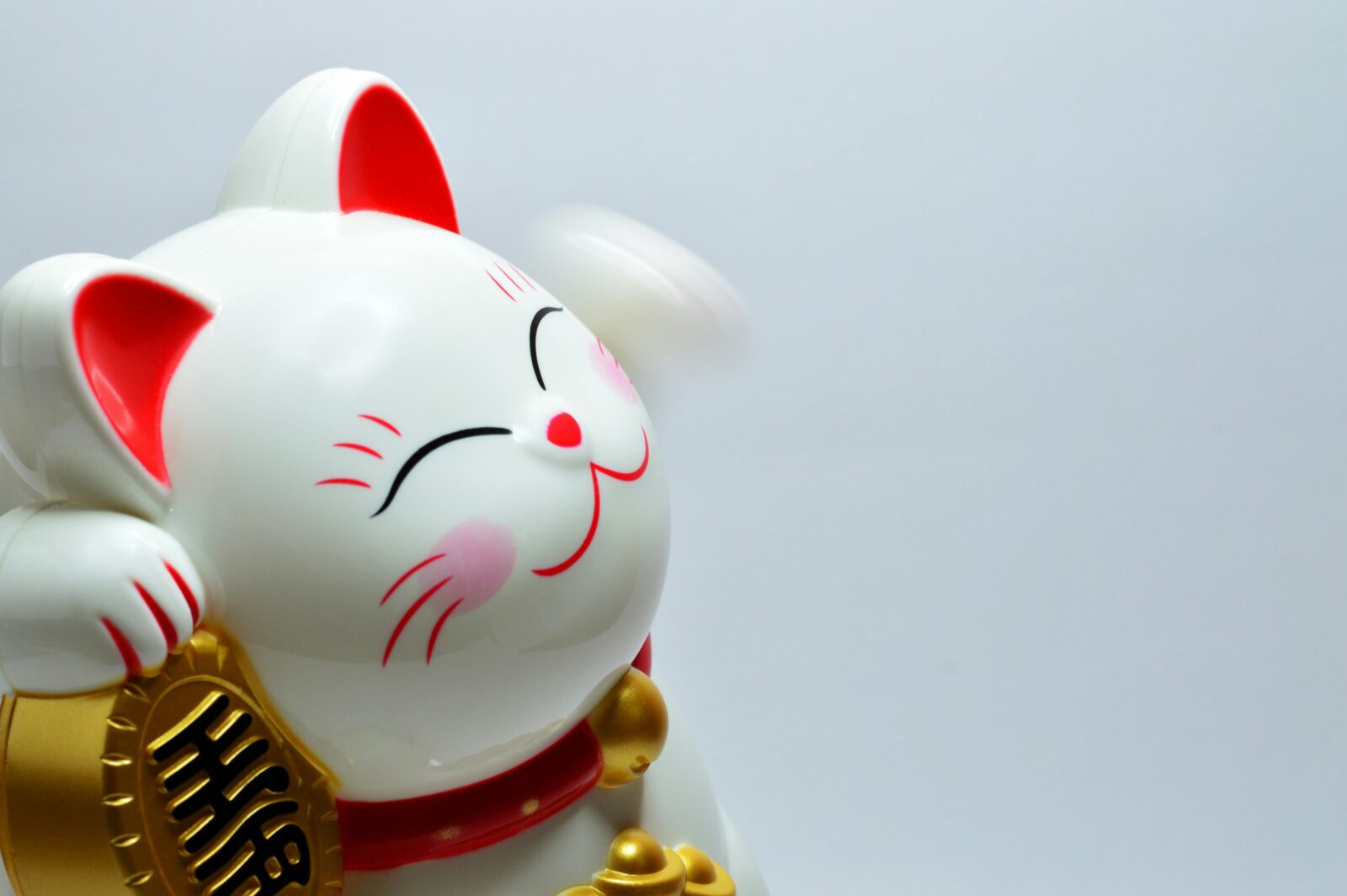 A close-up of a smiling white maneki-neko (lucky cat) figurine with red ears and gold coin, symbolizing good fortune and warm welcomes in Japan.