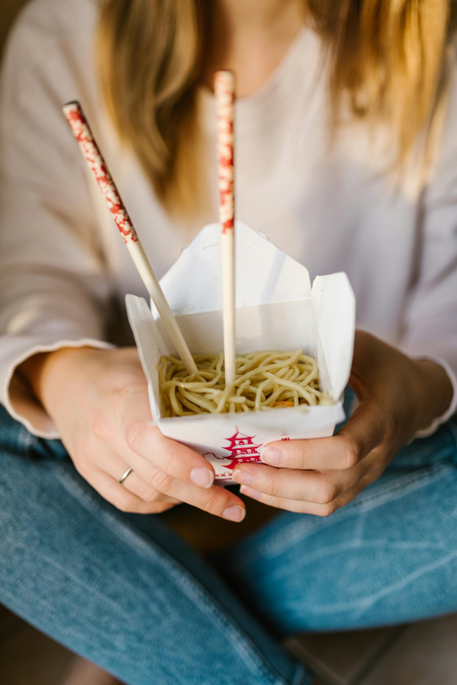 A person eating noodles with chopsticks from a takeout box, showing casual dining and everyday use of chopsticks.
