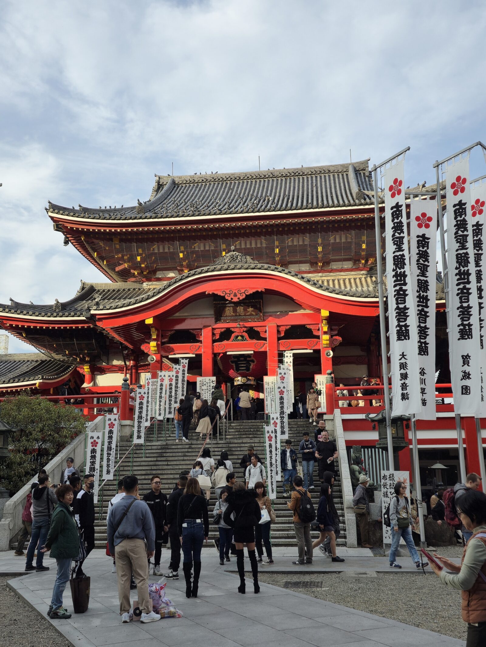 Red gate of Ōsu Kannon Temple in Nagoya with visitors praying and pigeons flying near the main hall.